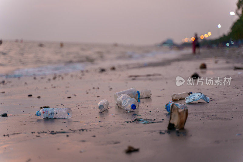 Low angle selective focus dirty beach with many consumer single used plastic waste along coast at twilight time. Environmental pollution micro plastic contamination problem concept.